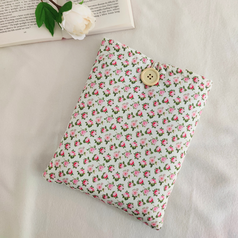 Floral book sleeve displayed on a white table next to an open book and a flower.